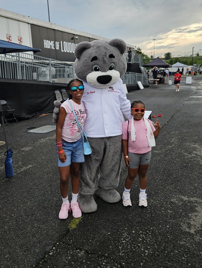 Dr. Bear and two girls pose for a photo outside Loudoun United FC field.