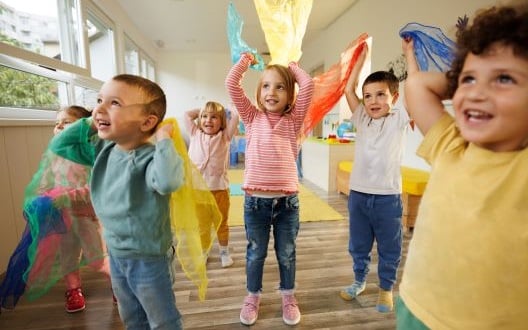 A group of kids at a party, smiling as they play with colorful scarves in the air