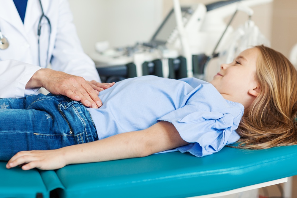 A healthcare provider examines a young girl's abdomen while the child lays on an examination table