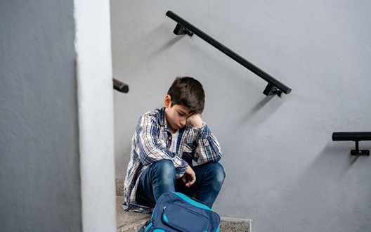 A boy sits on the stairs at school sadly holding his head