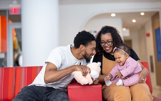 A couple and their toddler daughter sit in a doctor's office waiting room