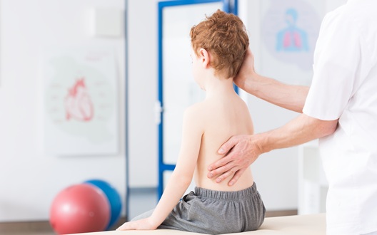 A healthcare provider examines a young boy sitting on a table in a doctor's office