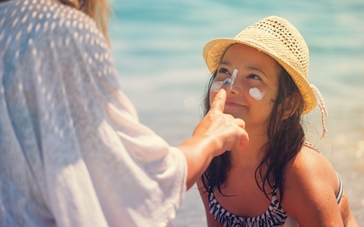 A mom at the beach applies sunscreen to her daughter's face