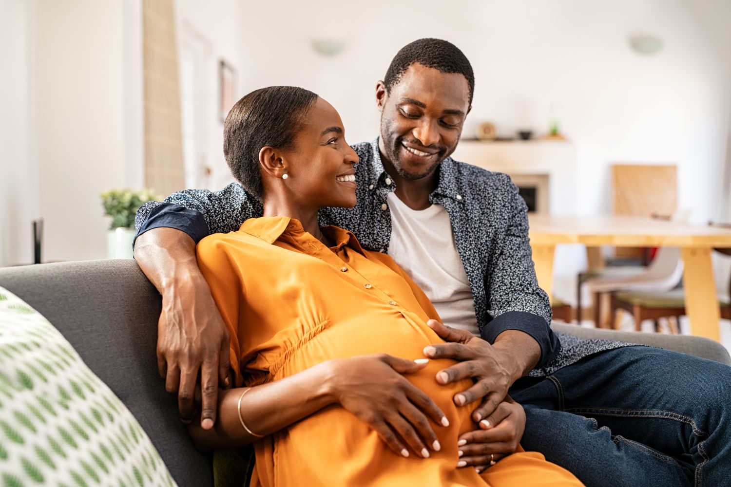 expecting parents sitting on couch and smiling at each other