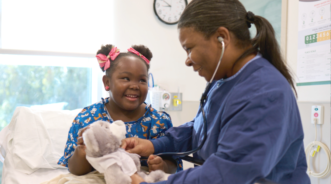 A female nurse and young patient happily examine a stuffed animal toy.