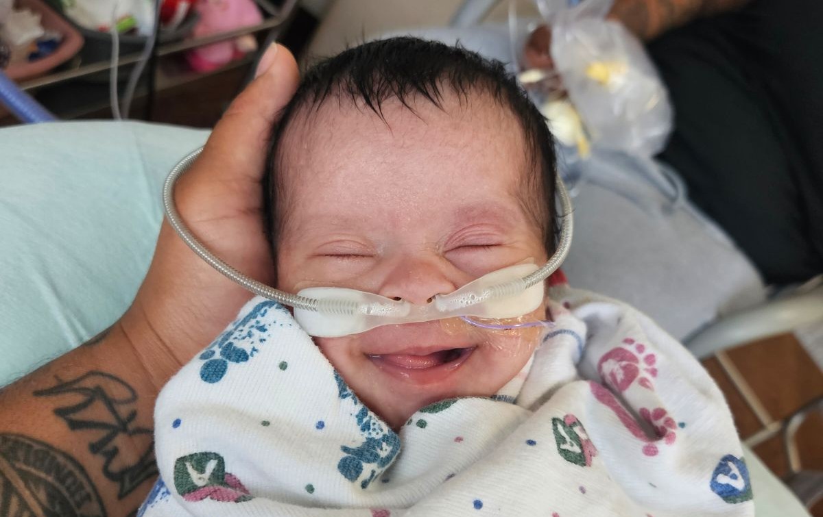 Infant Raya smiling while swaddled and receiving supplemental oxygen.