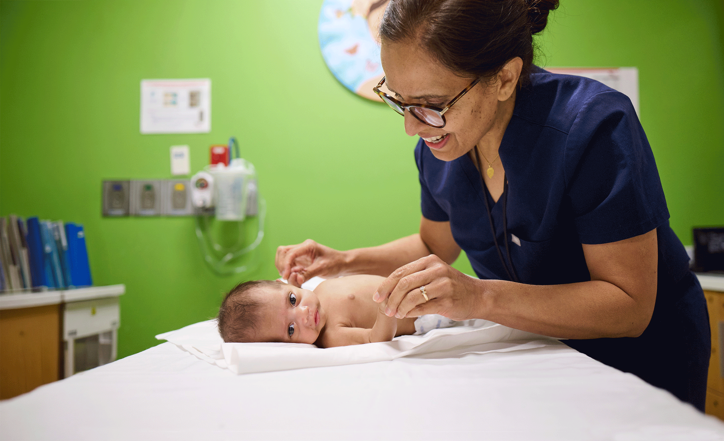 Woman smiling down at tiny infant on exam table.